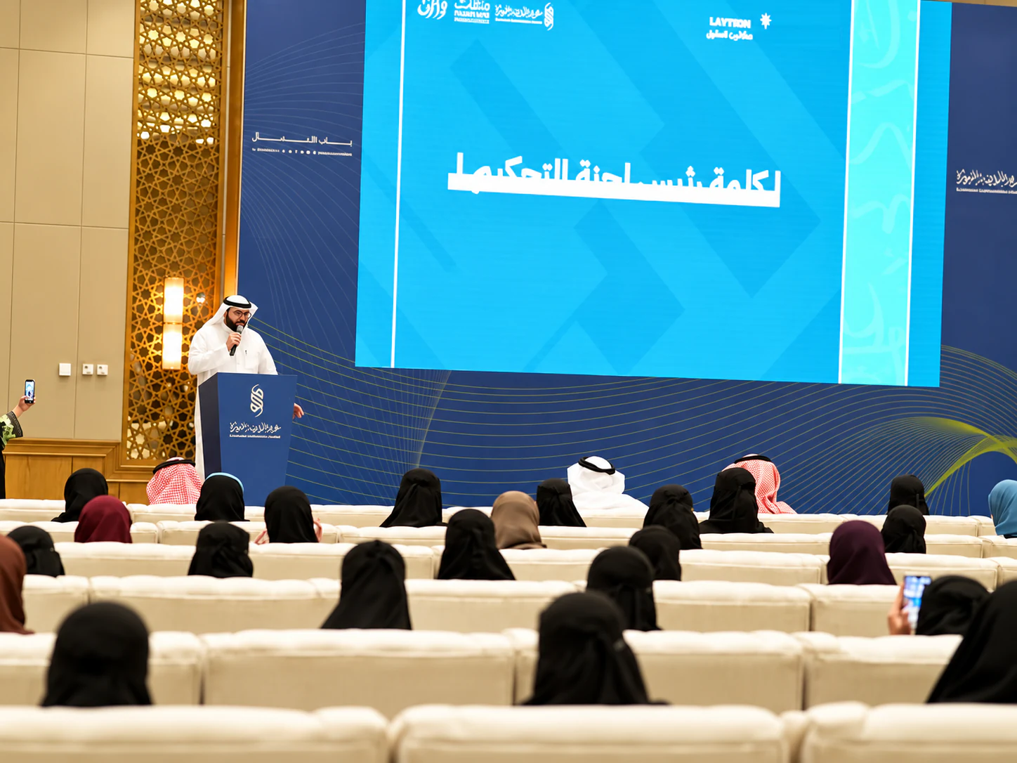 متحدث على المنصة أمام الحضور وخلفه شاشة كلمة رئيس لجنة التحكيم