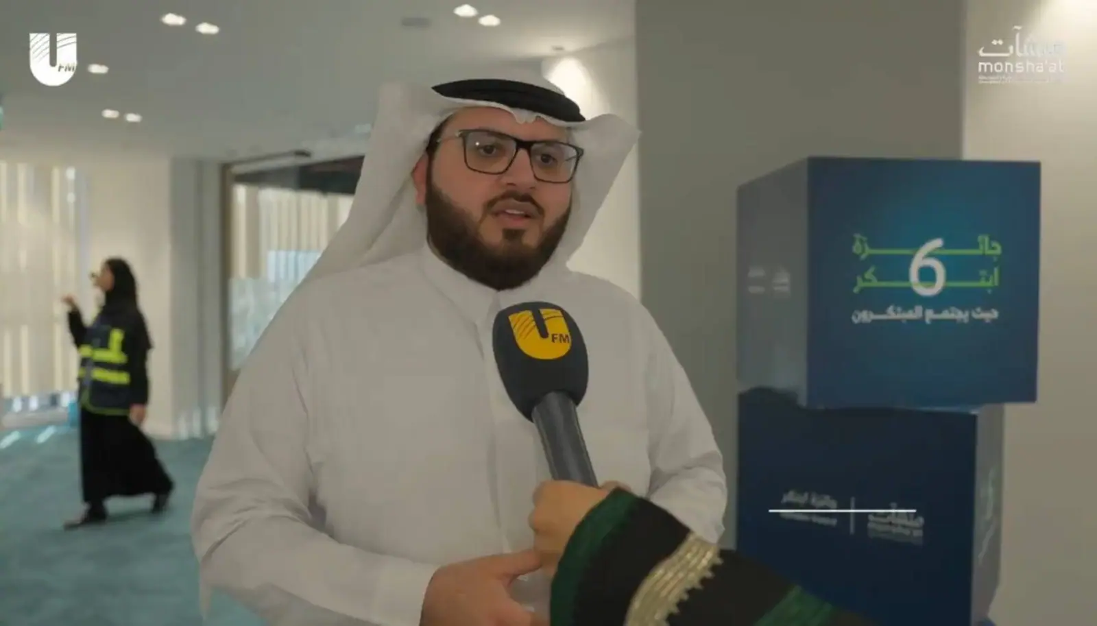 Ahmed Alshareef speaking into a UFM microphone, the Ebtaker Award branding behind him
